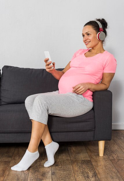 집에서 헤드폰으로 음악을 듣고 스마트 폰으로 웃는 임신 한 여자
