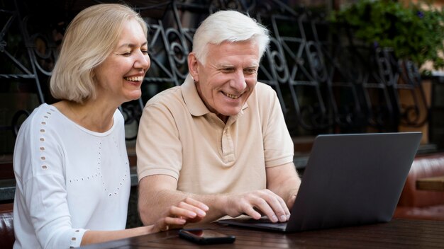 Smiley senior couple sitting down outdoors and looking and laptop