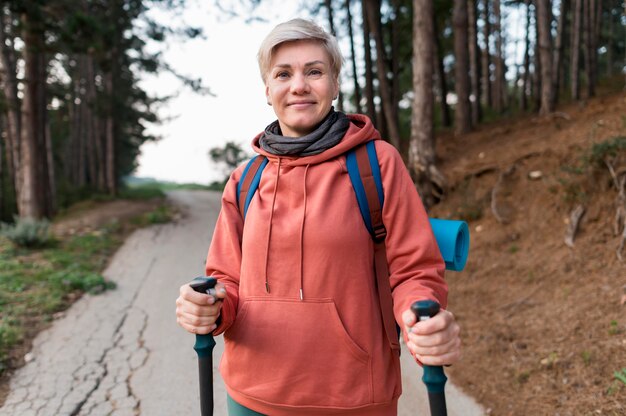 Smiley senior tourist woman with hiking sticks in the forest