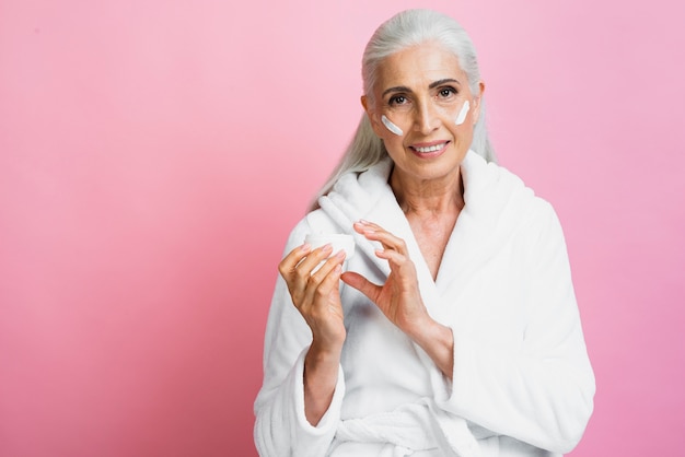 smiley senior woman applying moisturizer