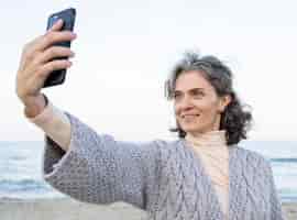 Free photo smiley senior woman taking a selfie by the beach