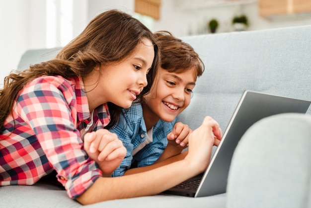 Smiley siblings on couch using laptop