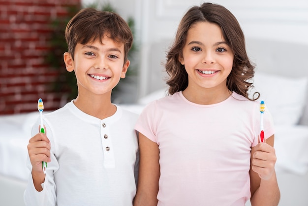Free photo smiley siblings at home holding toothbrush