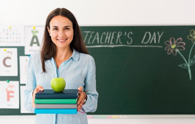 Smiley teacher holding a bunch of books and an apple with copy space