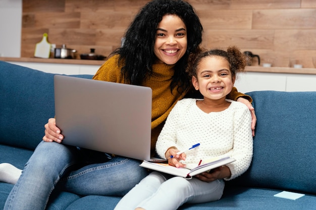 Smiley teenage girl helping little sister with online school on laptop