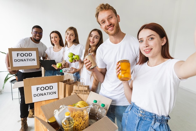 Smiley volunteers taking selfie together while preparing food for donation