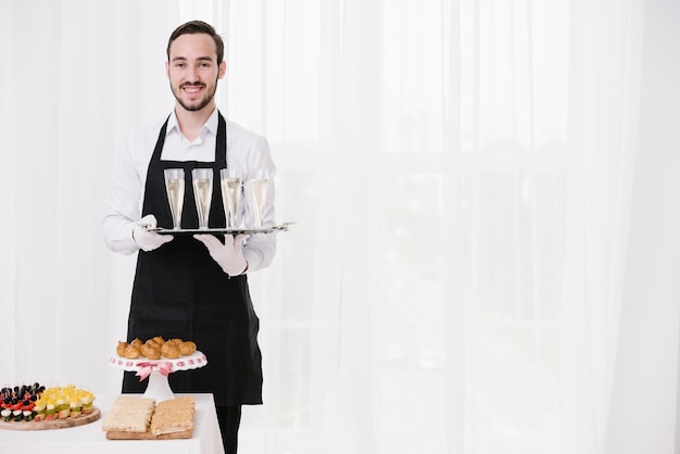 Smiley waiter holding glasses with copy space