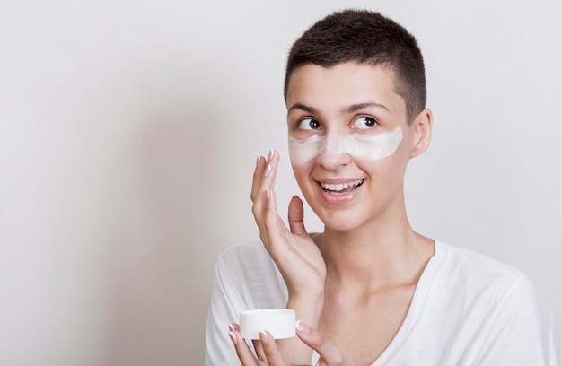 Free photo smiley woman applying cream on face
