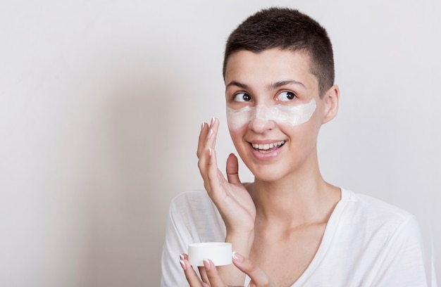 Smiley woman applying cream on face