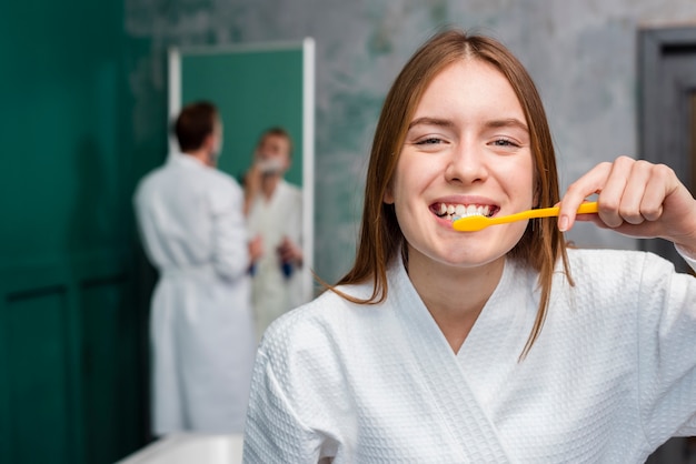 Smiley woman in bathrobe brushing her teeth