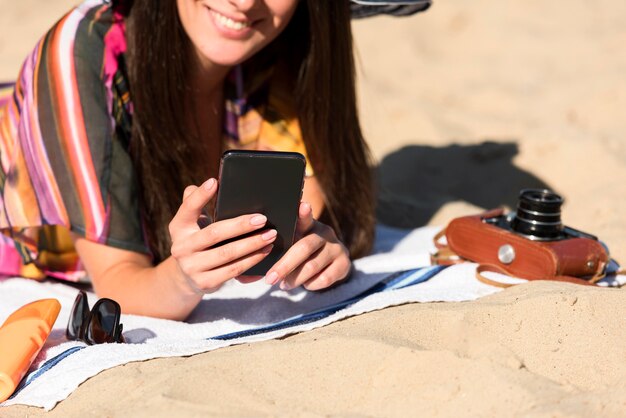 Smiley woman at the beach holding smartphone