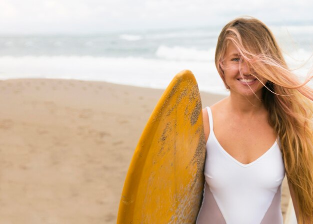 Smiley woman on the beach holding surfboard