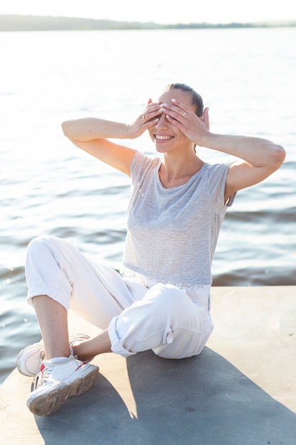 Smiley woman covering her eyes on dock