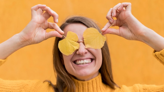 Free photo smiley woman covering her eyes with yellow leaves