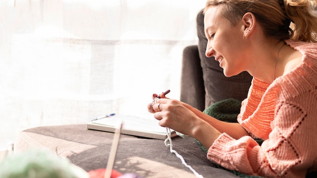 Free photo smiley woman crocheting indoors