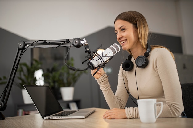 Smiley woman doing a podcast on radio with a microphone and laptop