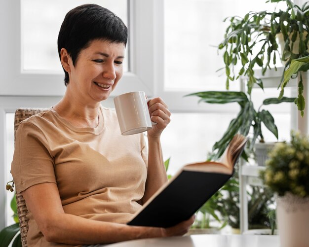 Smiley woman enjoying a book indoors with mug