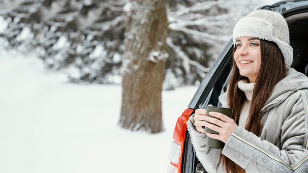 Smiley woman having a warm drink while on a road trip with copy space