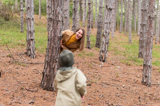 Улыбающаяся женщина прячется за деревом от сына