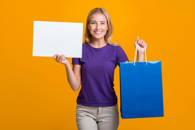 Free photo smiley woman holding blank sign and shopping bag