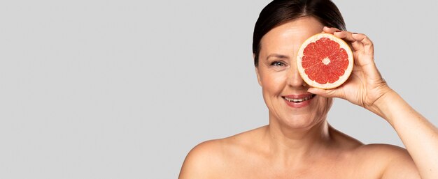 Smiley woman holding half of grapefruit over face with copy space
