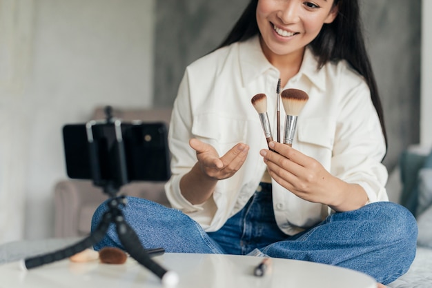 Smiley woman holding make up brushes while vlogging