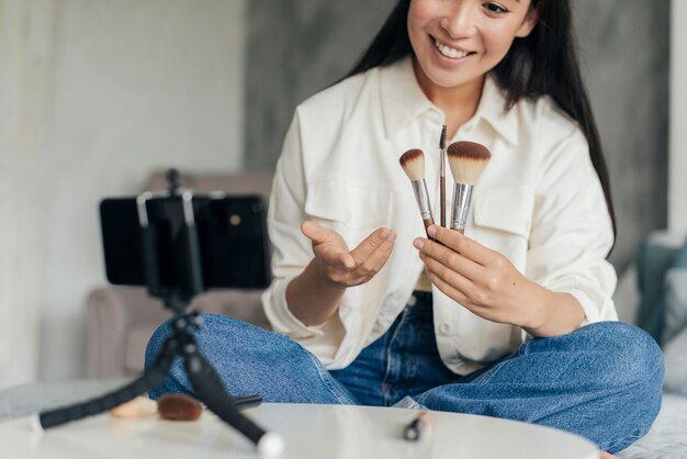 Smiley woman holding make up brushes while vlogging