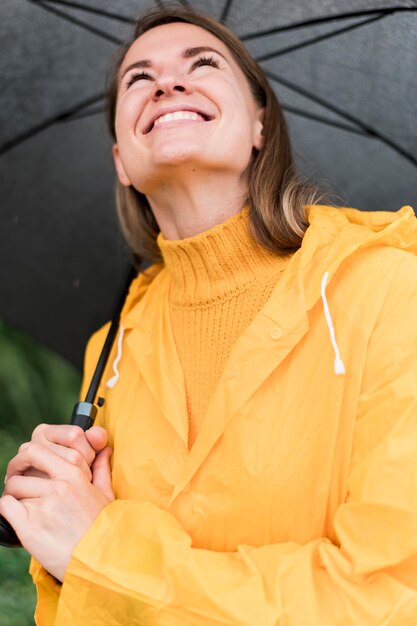 開いている黒い傘を屋外に保持しているスマイリー女性