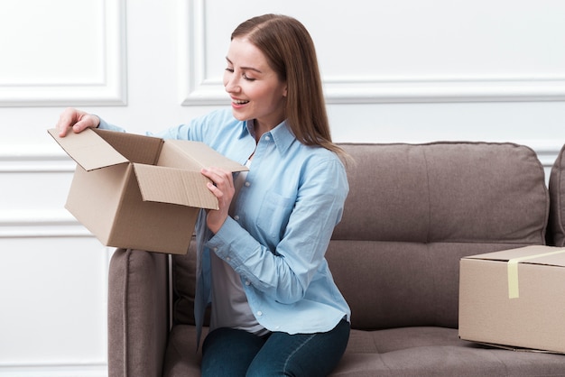 Smiley woman holding a package indoors and sitting on couch