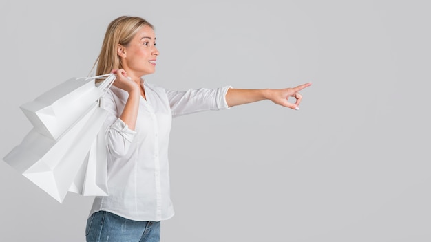 Smiley woman holding shopping bags and pointing to possible store sale