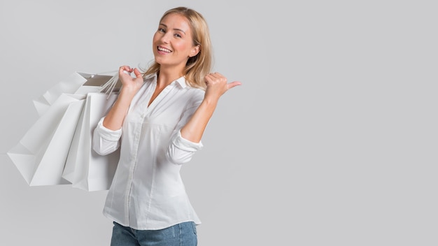 Smiley woman holding shopping bags and pointing behind to possible store sale