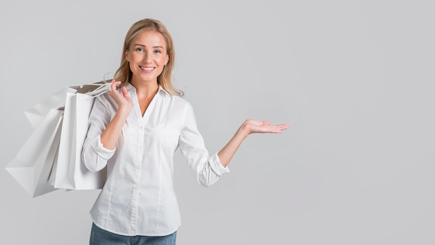 Smiley woman holding shopping bags and showing off space to her left