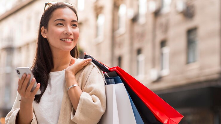 無料Photo 買い物袋とスマートフォンを屋外に保持しているスマイリー女性