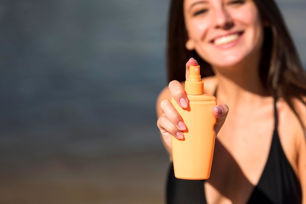 Smiley woman holding sunscreen at the beach with copy space