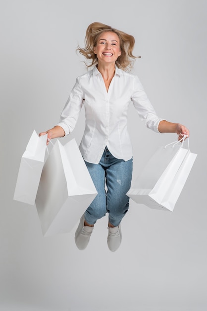 Donna sorridente che salta e posa mentre si tiene un sacco di borse della spesa