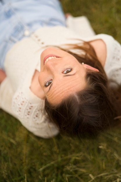 Free photo smiley woman laying on grass high angle