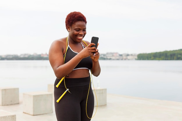 Foto gratuita donna sorridente guardando smartphone durante l'allenamento all'aperto