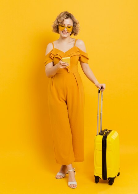 Smiley woman looking at smartphone while holding luggage