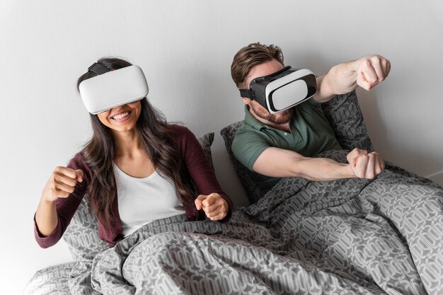 Smiley woman and man using virtual reality headset in bed