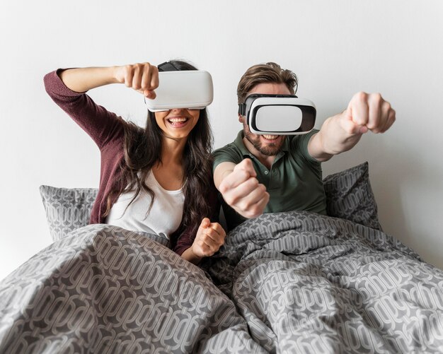 Smiley woman and man using virtual reality headset in bed