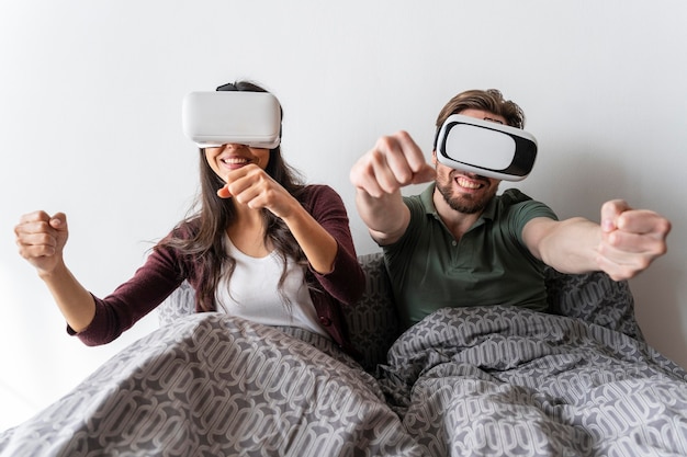 Smiley woman and man using virtual reality headset in bed