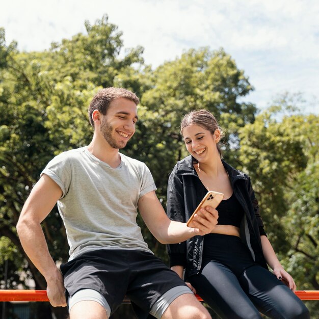 Smiley woman and man with smartphone outdoors while exercising