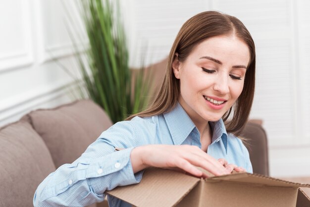 Smiley woman opening a package indoors
