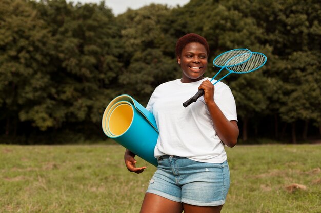 Smiley woman outdoors with rackets and yoga mat