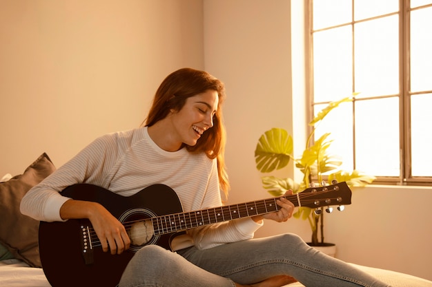 웃는 여자 집에서 침대에서 기타를 연주