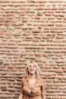 Бесплатное фото Смайлик женщина позирует против кирпичной стены с копией пространства