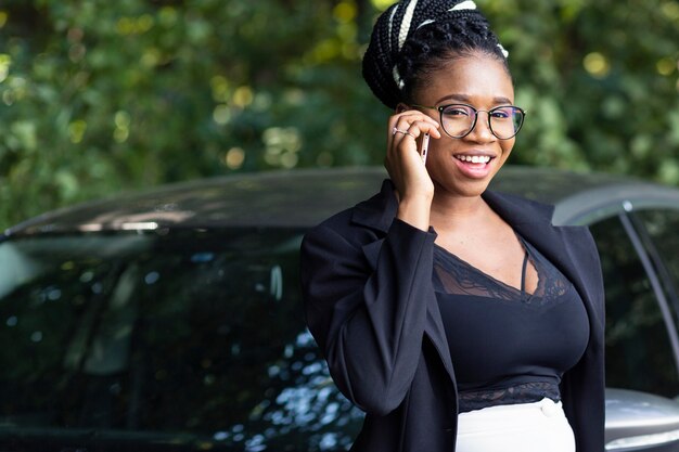 Smiley woman posing next to car while talking on smartphone