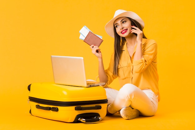 Smiley woman posing next to luggage while holding plane tickets and passport