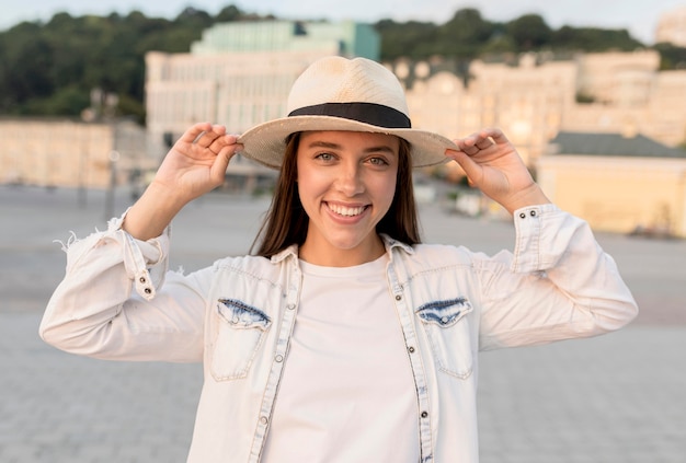 Smiley woman posing outdoors with hat while traveling