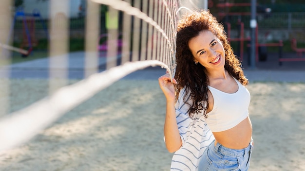 Foto gratuita donna sorridente in posa accanto a un campo da pallavolo all'aperto